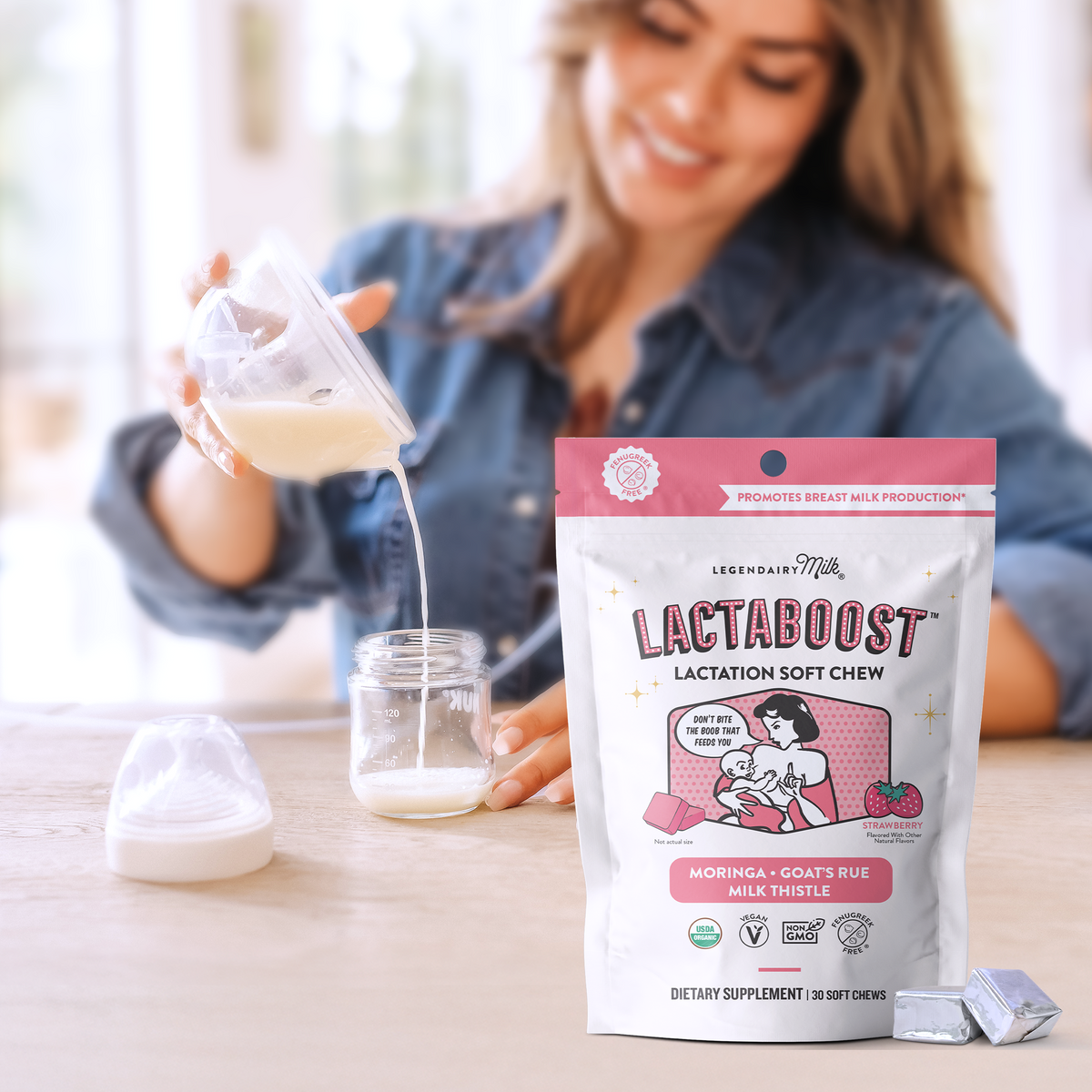 A woman in a denim shirt is shown in a bright kitchen setting, pouring milk from a glass container into a small jar. In the foreground, a bag of Lee-Brain & Milk Lactaboost Lactation Soft Chew supplements is prominently displayed on a light wooden table, with two silver foil packets beside it.